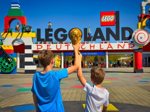 Samy und Tobi halten den offiziellen LEGO Pokal der FIFA Fußball-Weltmeisterschaft in die Höhe und freuen sich schon auf das neue Fußballevent FIFA World Cup 2026 Experience vom 11. Juni bis 19. Juli in den LEGOLAND Resorts.